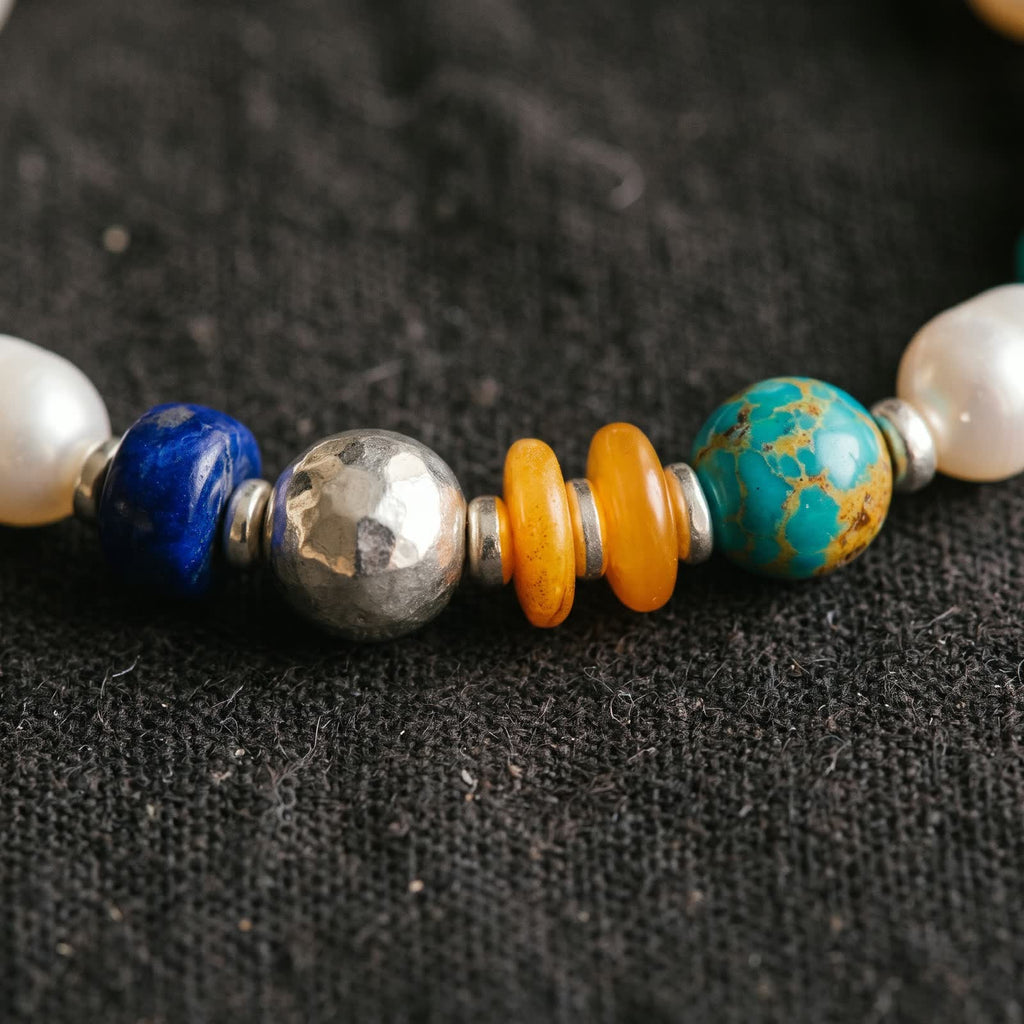 Close-up of the coloured beads: a deep blue rondelle, a large hand-hammered 925 sterling silver bead, two honey-orange discs and a blue-green bead with golden veins, between white pearls