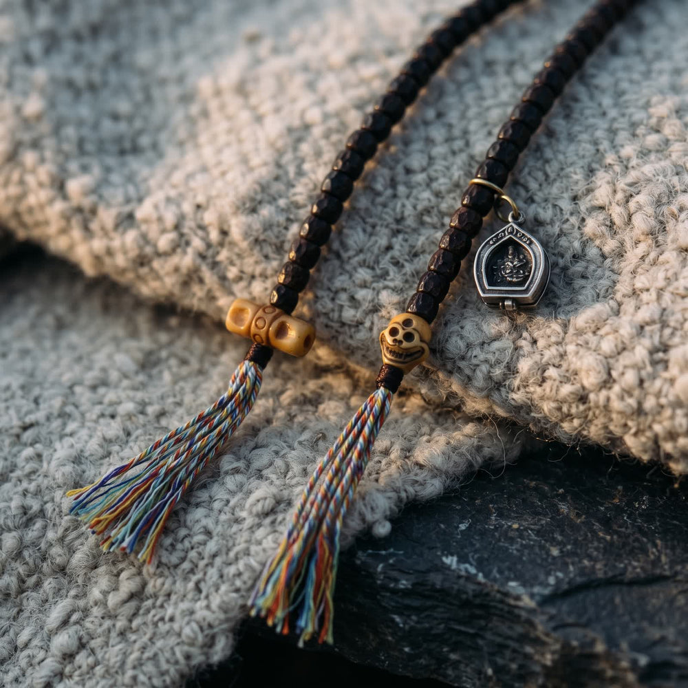 Two counter strings ending in a carved bone bead and a bone skull bead, five-color tassels and a small gau box, on undyed wool