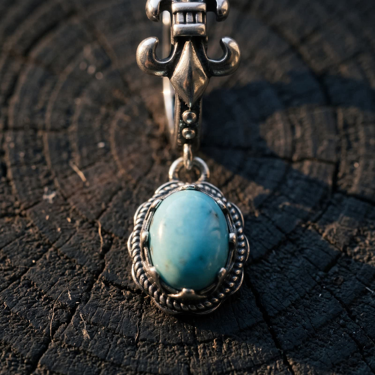 Close-up of an oval sky-blue turquoise in a twisted-rope sterling silver frame below a fleur-de-lis