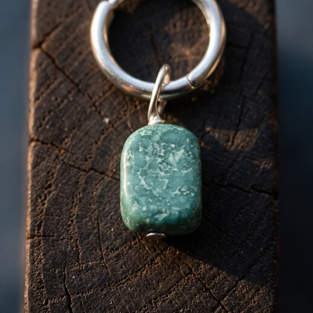 Close-up of a green stone drop with pale speckled markings hanging from a small polished hoop