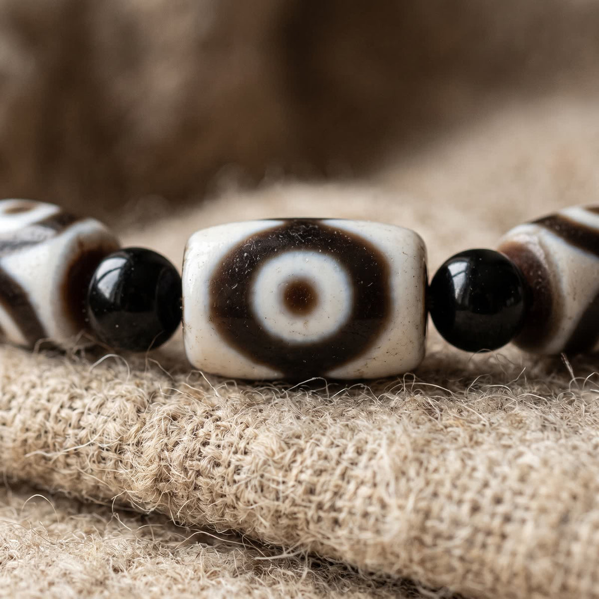Close-up of a white agate dzi bead with a brown-ringed eye between two black agate beads