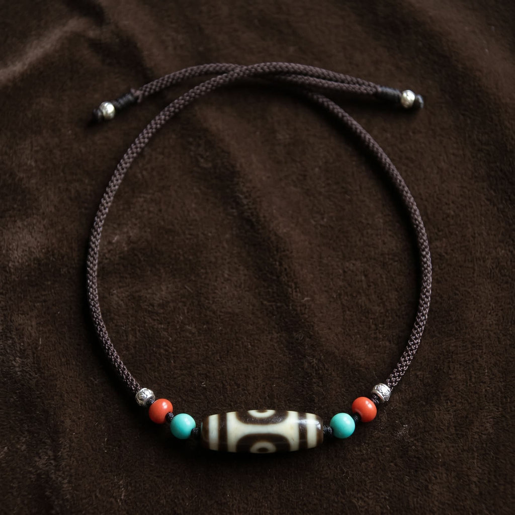 Full-length flat lay of the two-eyed agate dzi necklace on dark brown velvet, showing the braided cord and the two adjustable sliding knots with beads
