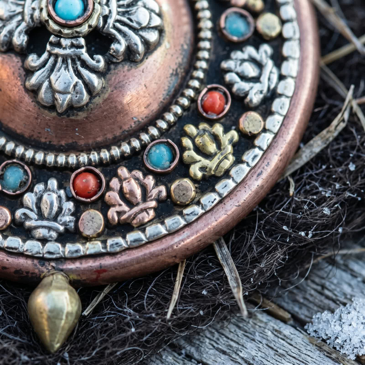 Close-up of silvery, golden and copper-red lotus appliqués alternating with red stones and stabilized turquoise on the copper gau box