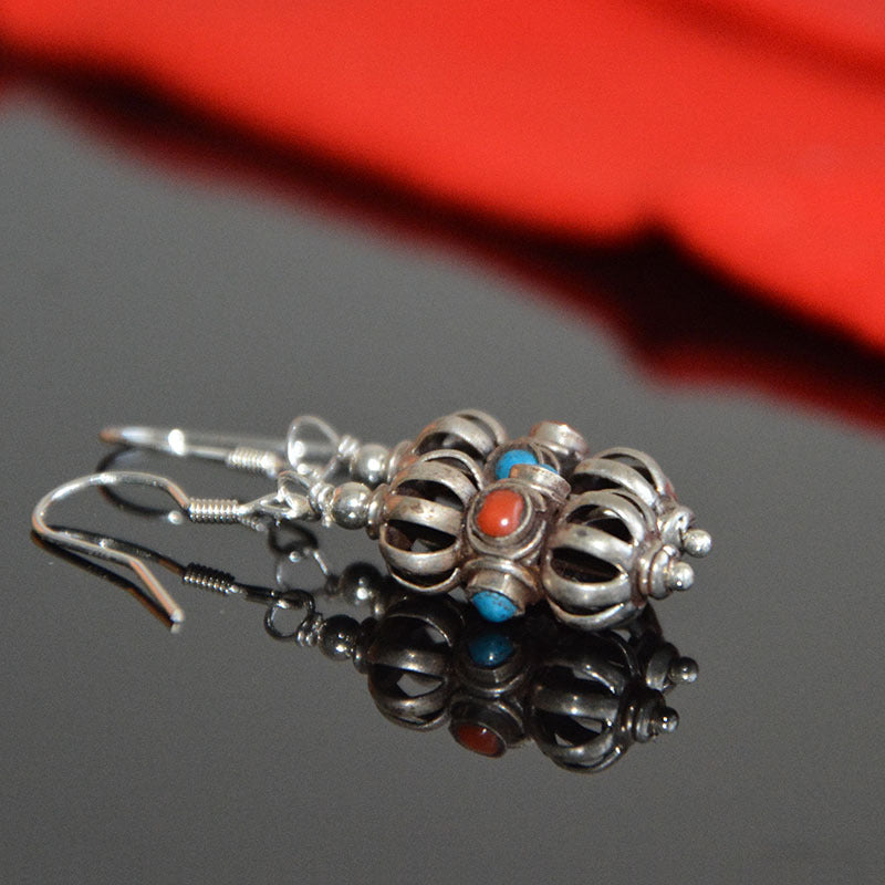 Vajra drop earrings lying on their side on dark glass, a red stone between blue stones