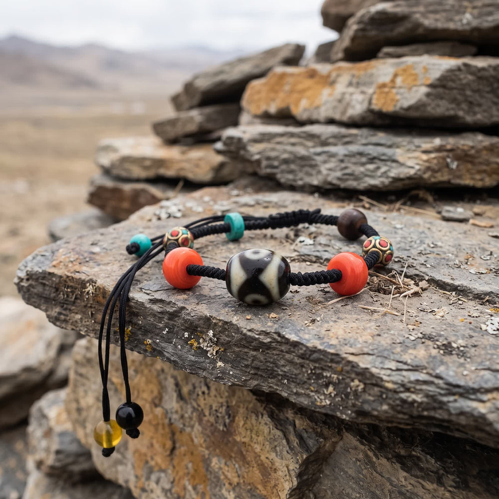 Dalo dzi cord bracelet on a stack of flat slate stones, its two cord tails with small end beads hanging over the edge