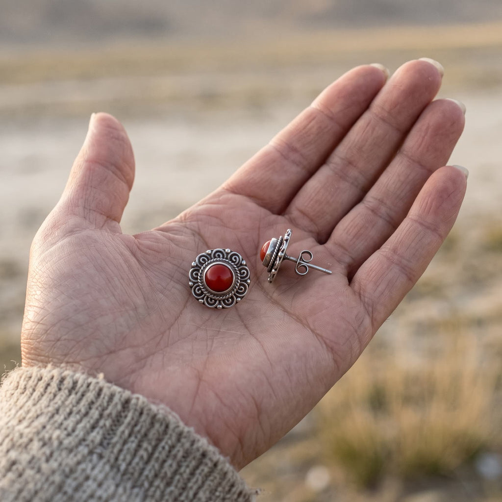 Pair of red stone filigree stud earrings in an open palm, one turned on its side to show the post and butterfly back