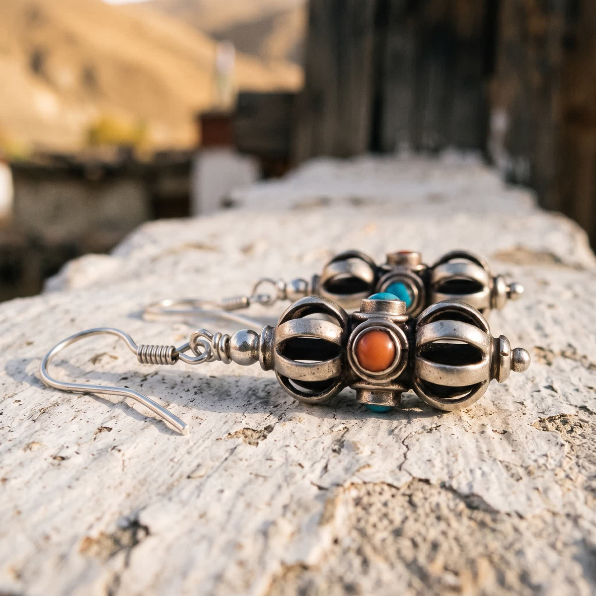 Vajra drop earring lying on its side on a whitewashed stone wall, a red stone facing up between blue stones
