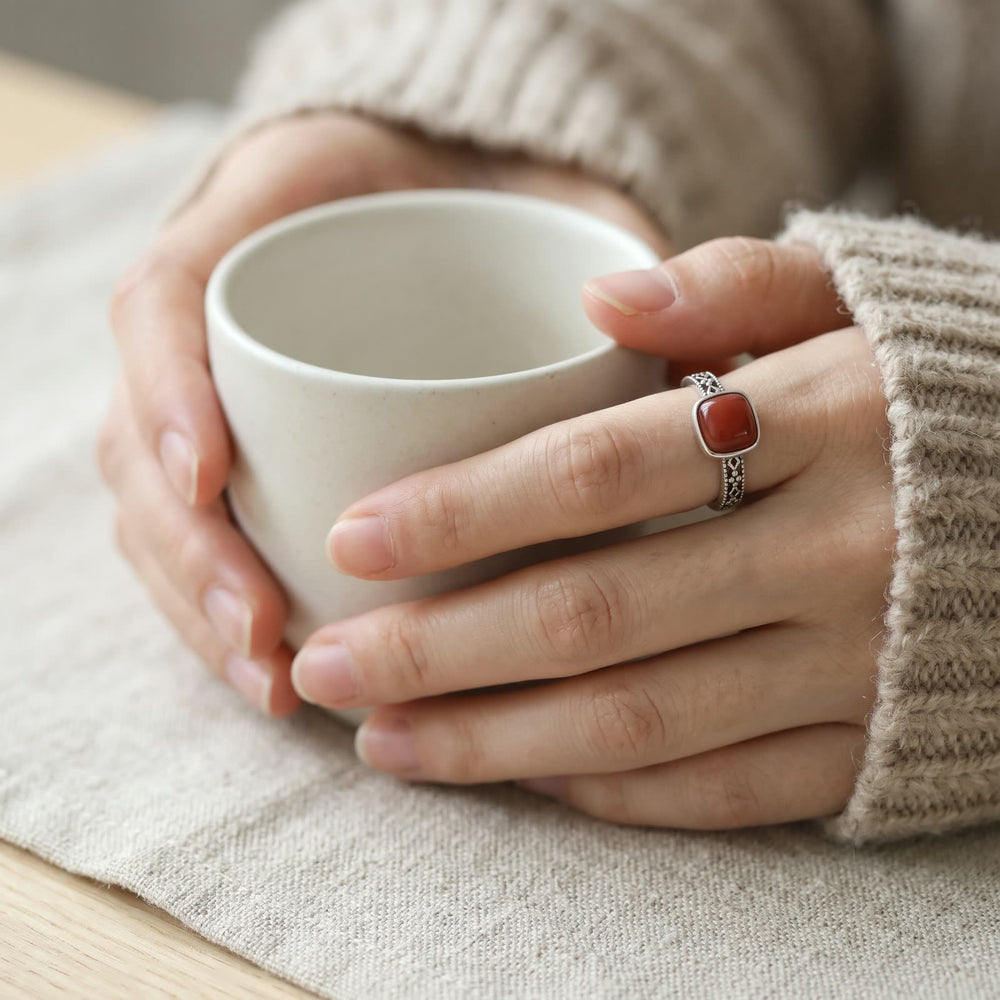Hands holding a white ceramic cup, a ring with a square red stone and openwork band on the index finger
