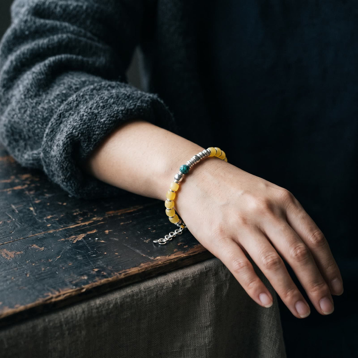 Honey-yellow bead and turquoise bracelet with sterling silver beads worn on a woman's wrist, extender chain hanging at the side