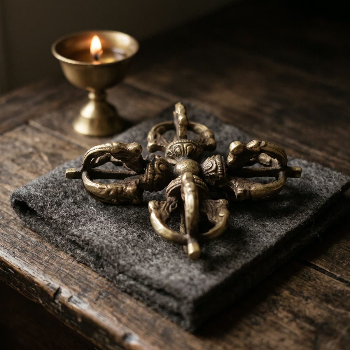 Double vajra on folded charcoal wool felt on an old wooden altar table beside a small butter lamp