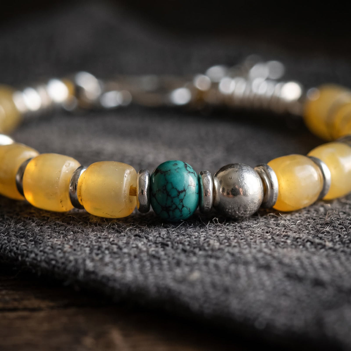 Close-up of translucent honey-yellow barrel beads, the turquoise bead and a polished sterling silver ball