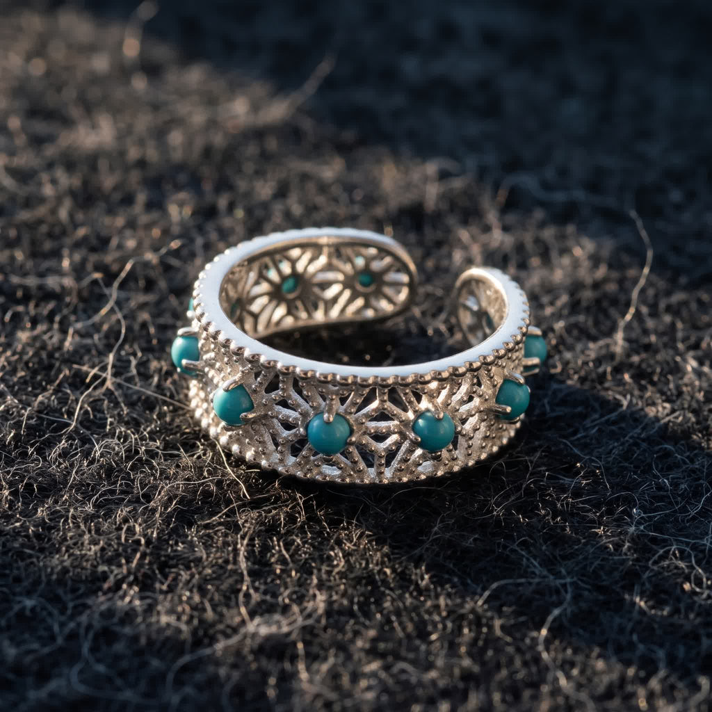 Adjustable openwork silver ring with blue-green stones lying on dark charcoal wool felt in warm side light