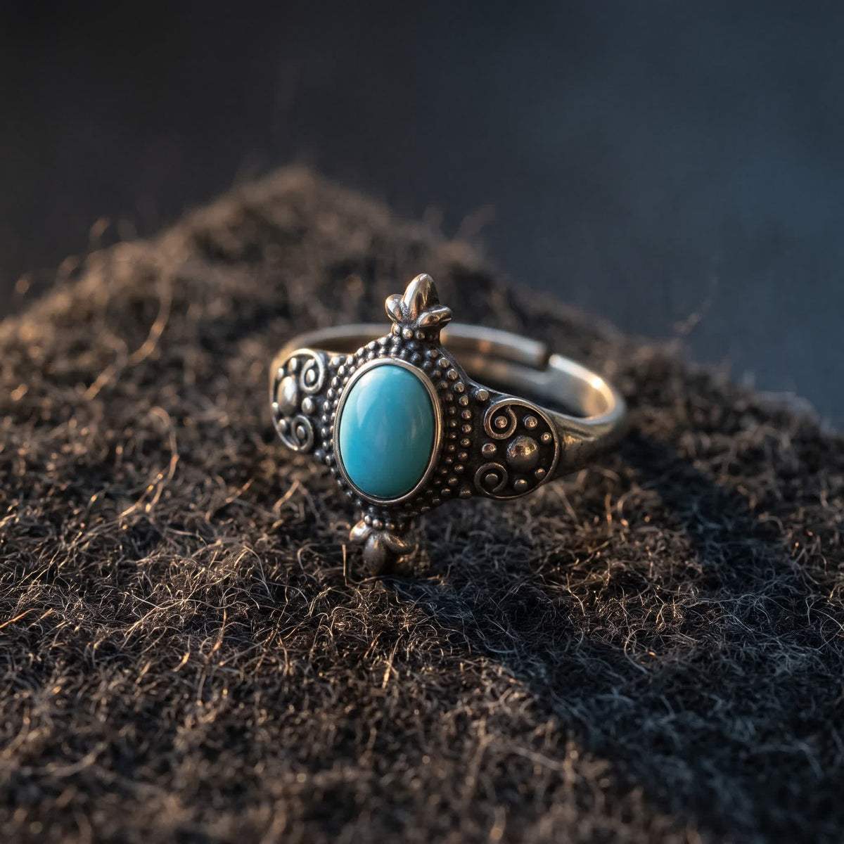 Adjustable oval turquoise ring with granulated detailing lying on dark charcoal wool felt in warm side light