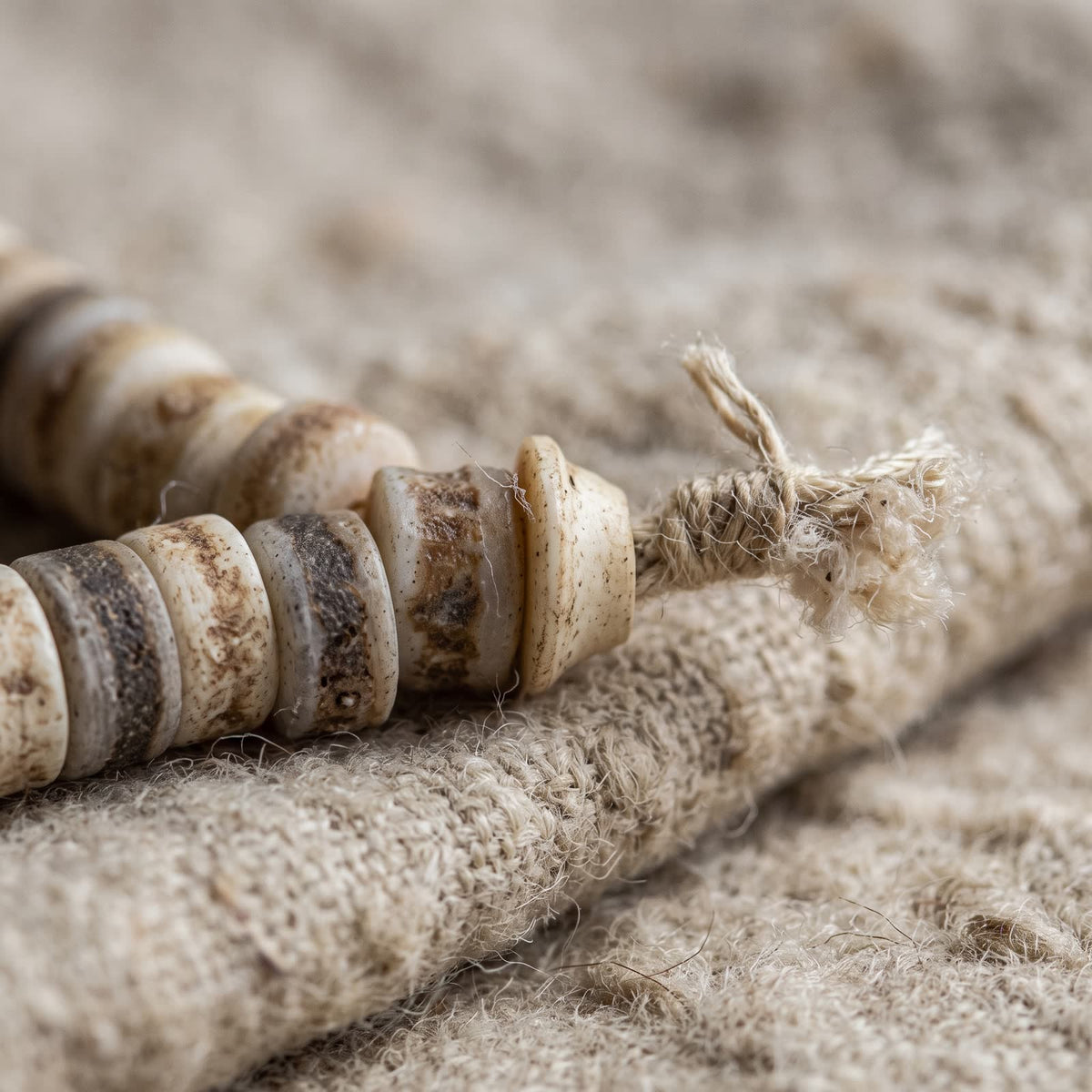 Close-up of the mala's hemp twine knot and frayed tuft beside the last bone beads