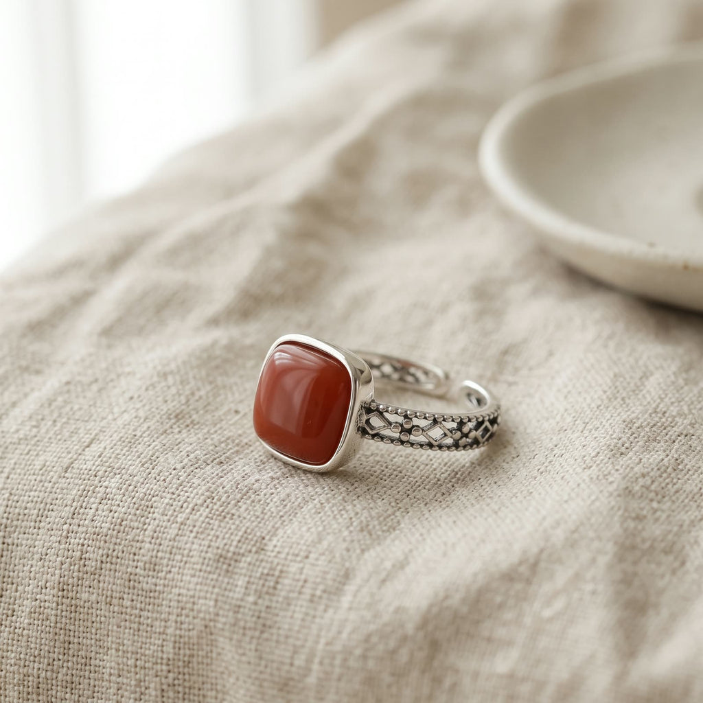 Ring with a square red stone and openwork band lying on soft oatmeal linen beside a small ceramic dish