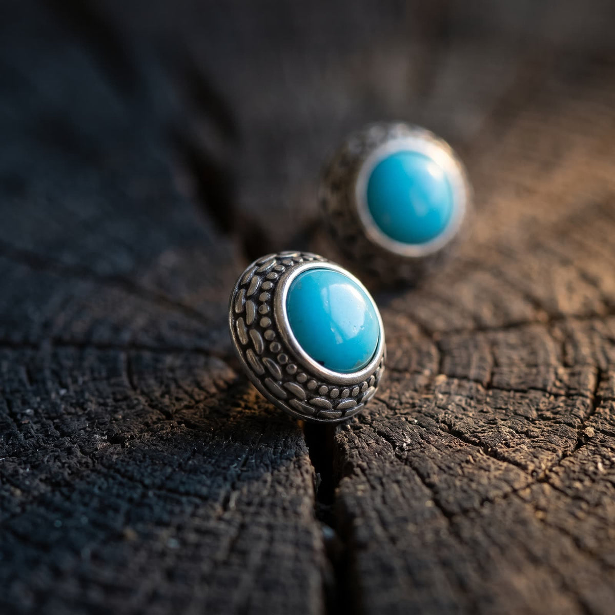 Side view of a turquoise stud earring showing the domed stone and the sloping patterned silver bezel