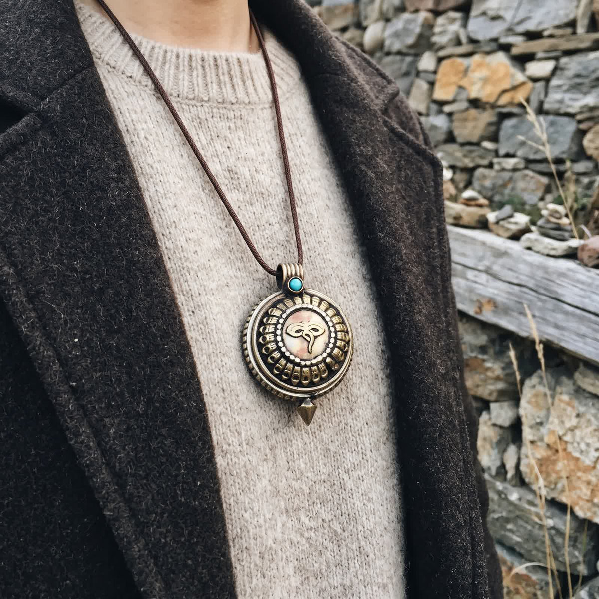 Gau box pendant with Buddha eyes worn on a thin dark cord over an oatmeal wool sweater and charcoal jacket