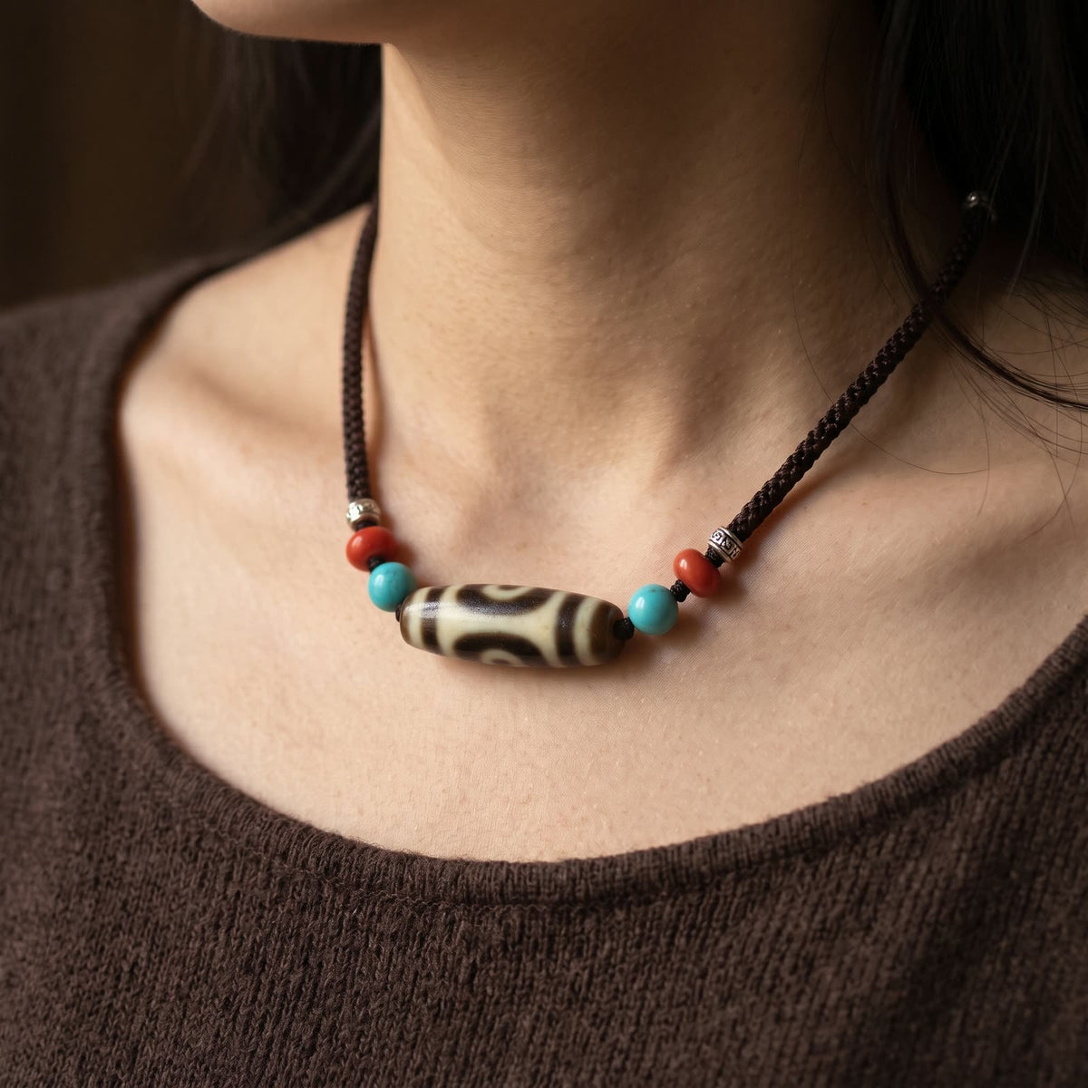 Two-eyed agate dzi bead necklace worn short at the collarbones over a dark brown knit top