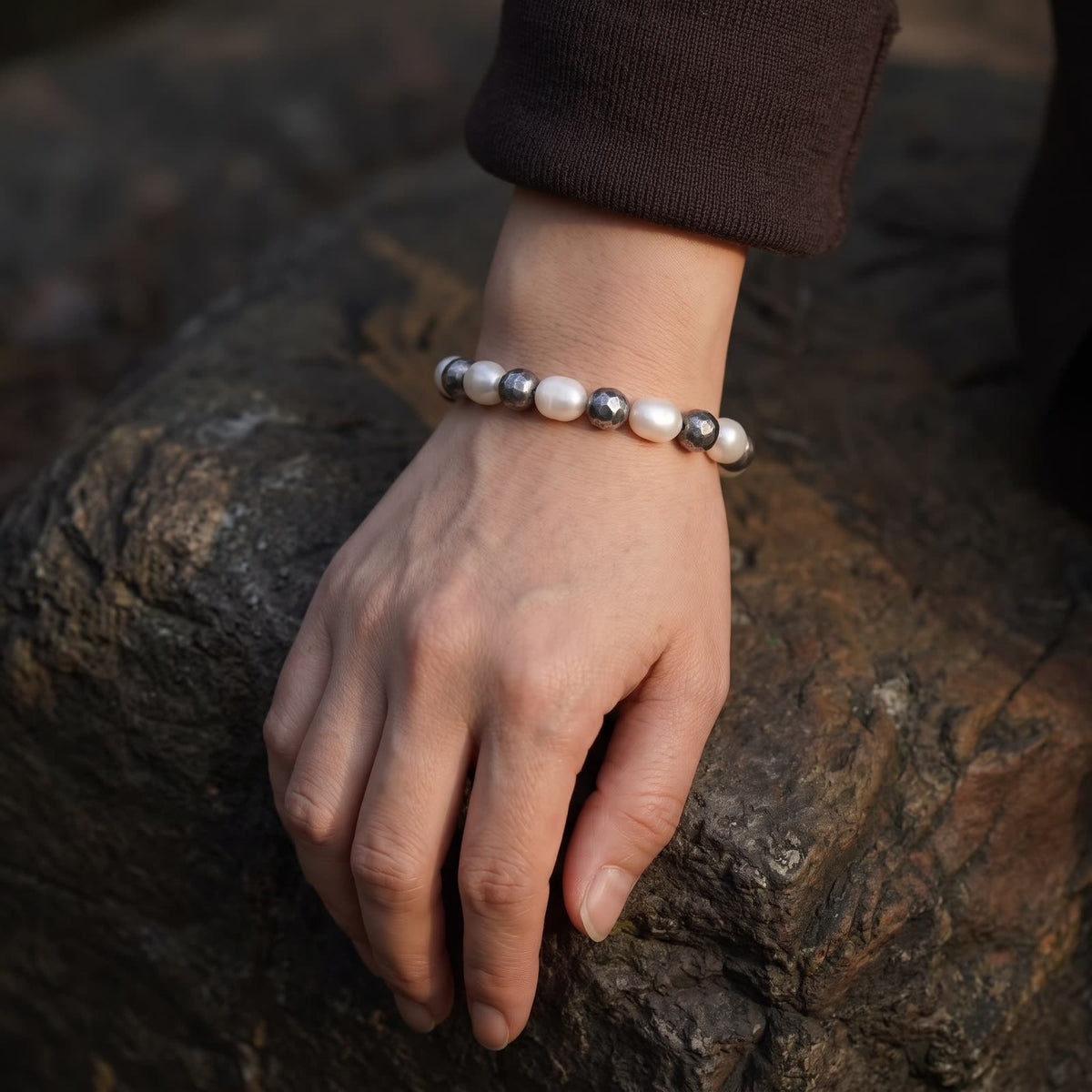 Pearl and hammered silver bead bracelet worn on a wrist resting on dark rock