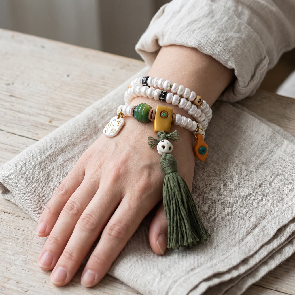 Pearl-white bead mala wrapped three times around a woman's wrist, the squared guru bead, openwork white bead and dark green tassel hanging beside the hand