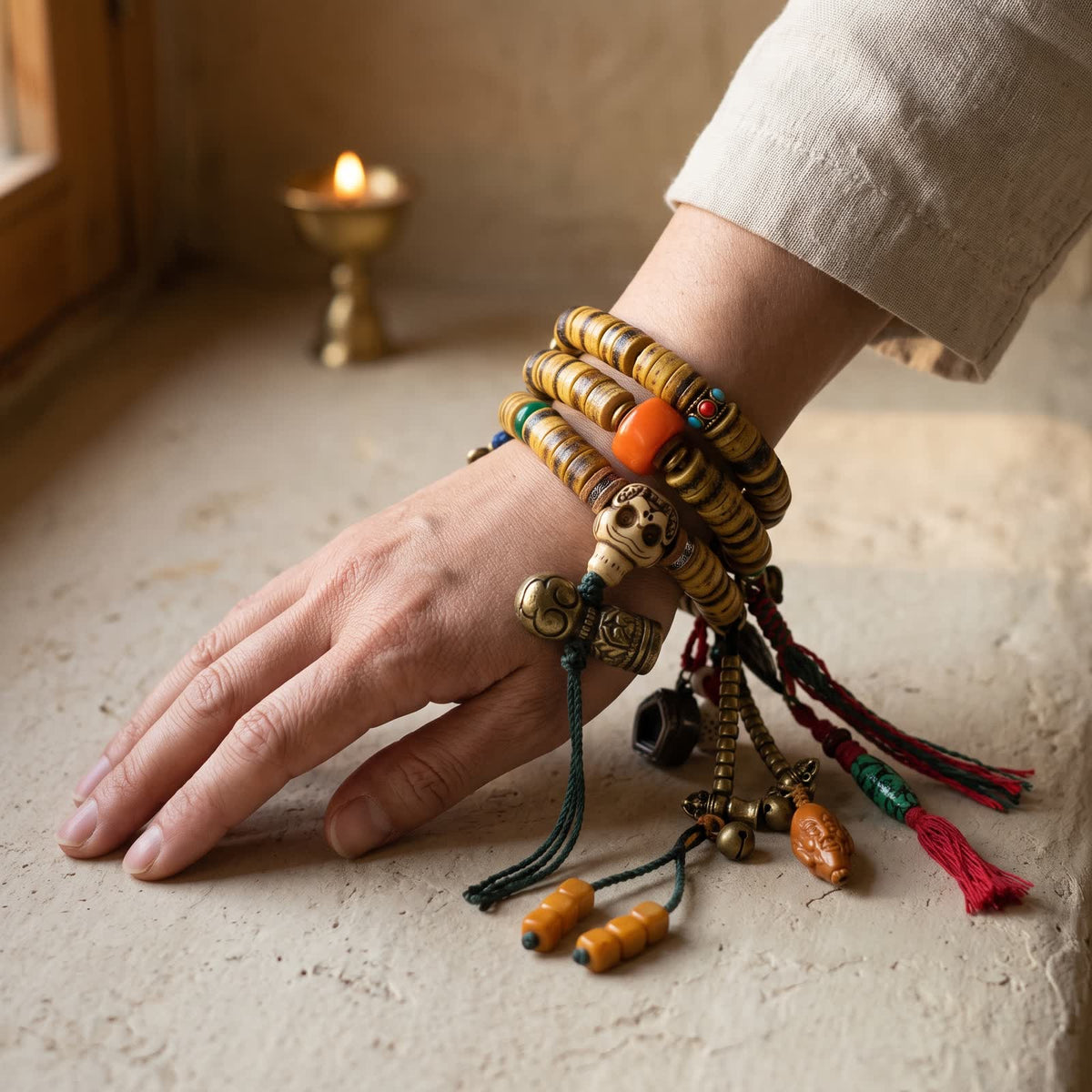 Bone disc mala wrapped three times around a woman's wrist, skull guru bead on top with amber cube beads, charms and tassels falling beside the hand
