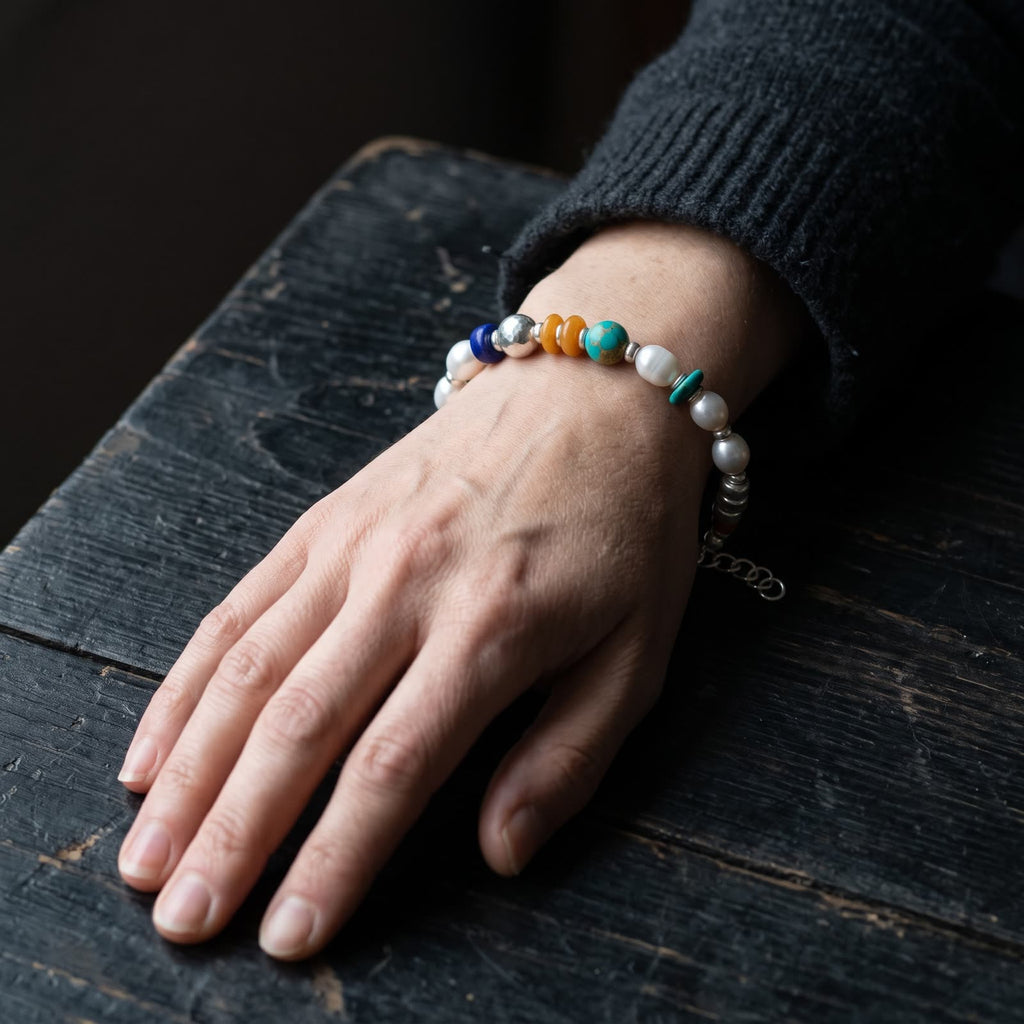 Pearl and mixed bead bracelet worn on a woman's wrist, the hand resting on a dark wooden table, coloured beads on top of the wrist