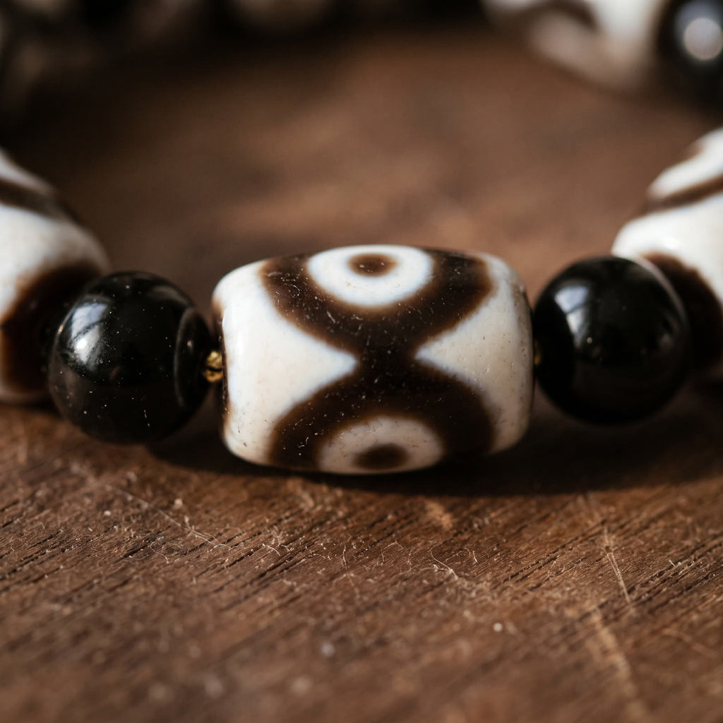 Close-up of an agate dzi bead showing its crossed brown bands and half eyes, beside black agate beads