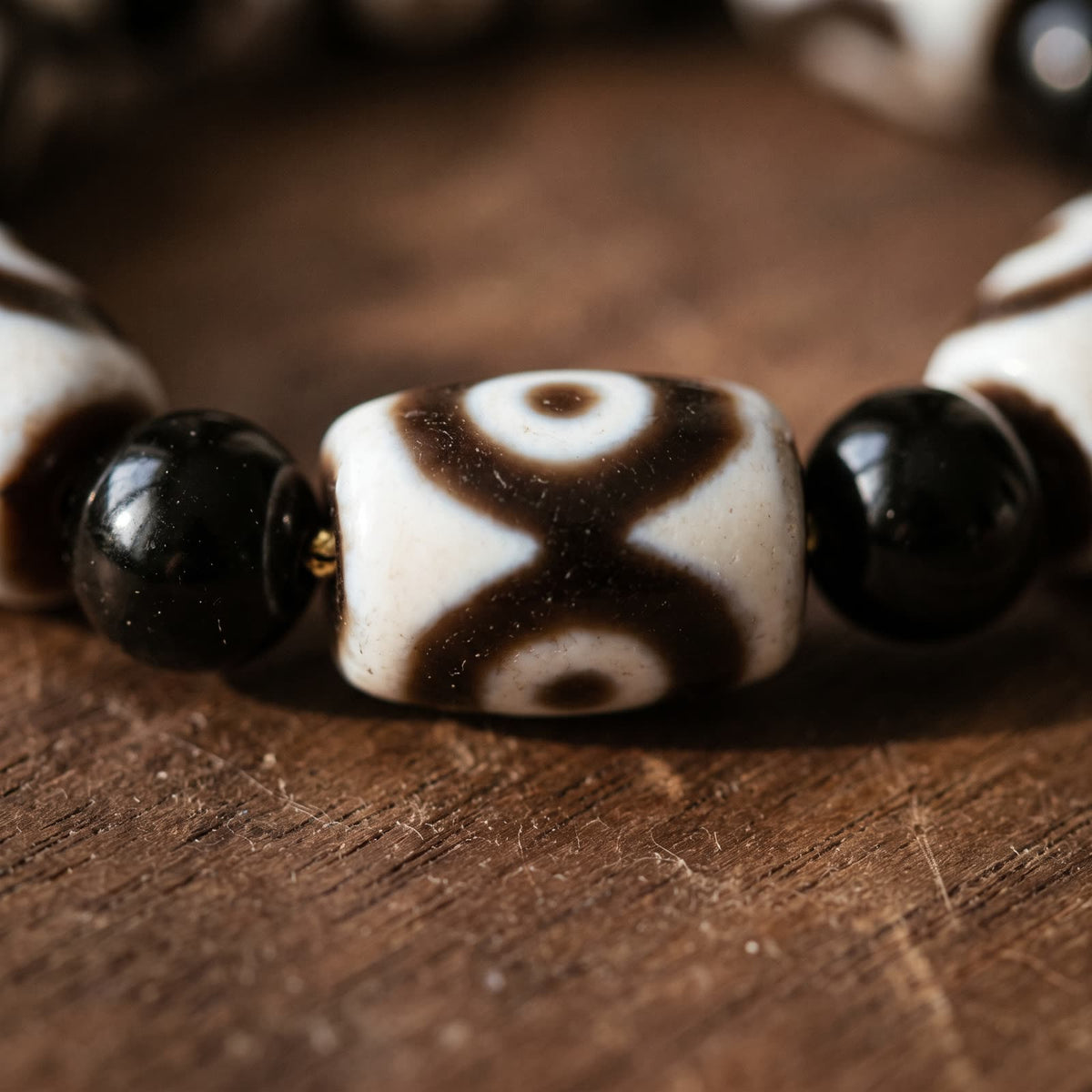Close-up of an agate dzi bead showing its crossed brown bands and half eyes, beside black agate beads