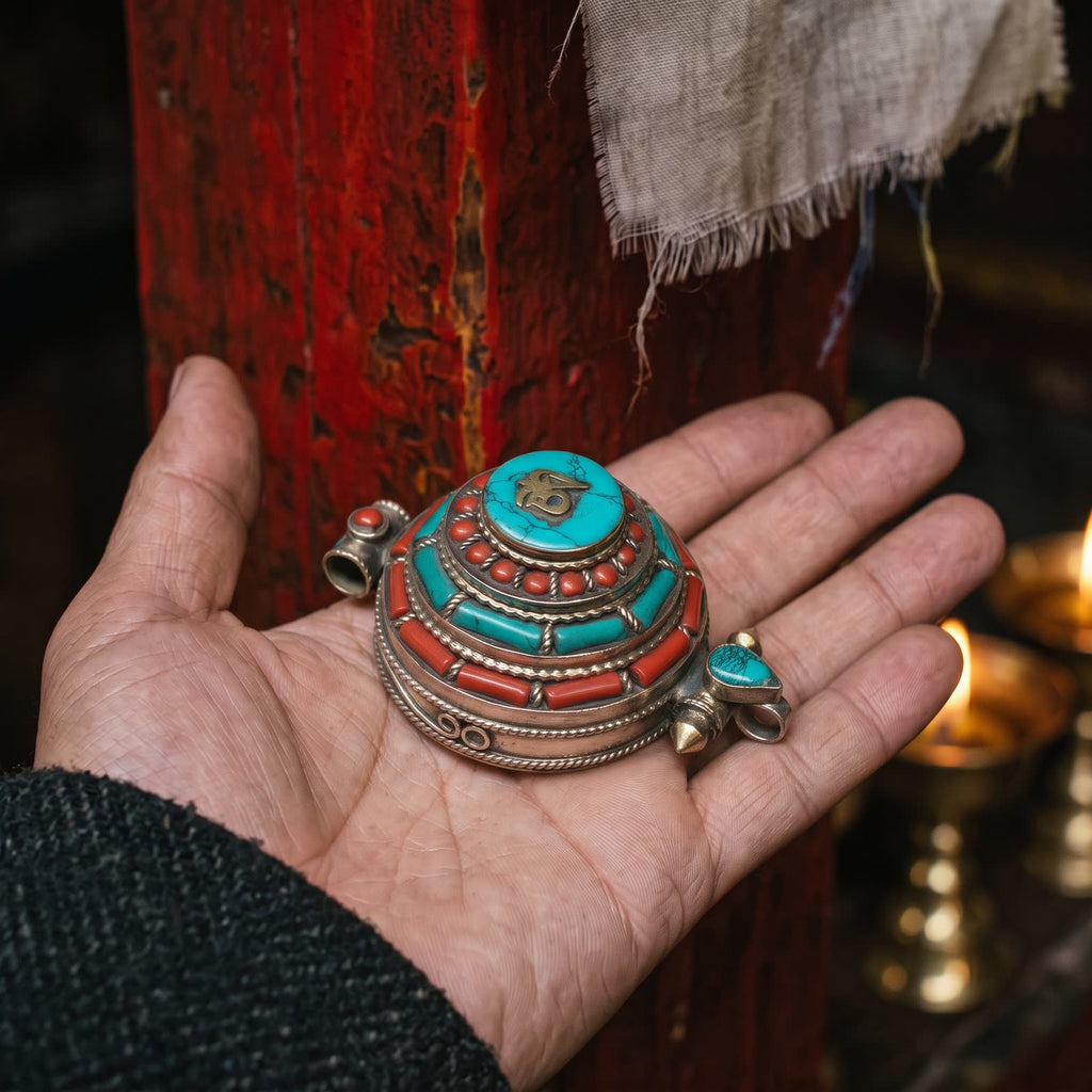 Gau box pendant with stabilized turquoise and red stones resting in an open palm in warm butter-lamp light