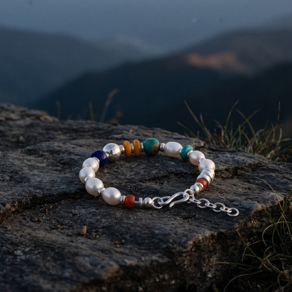 Pearl bracelet lying on a dark rock ledge at dusk, layered blue mountain ridges softly out of focus behind