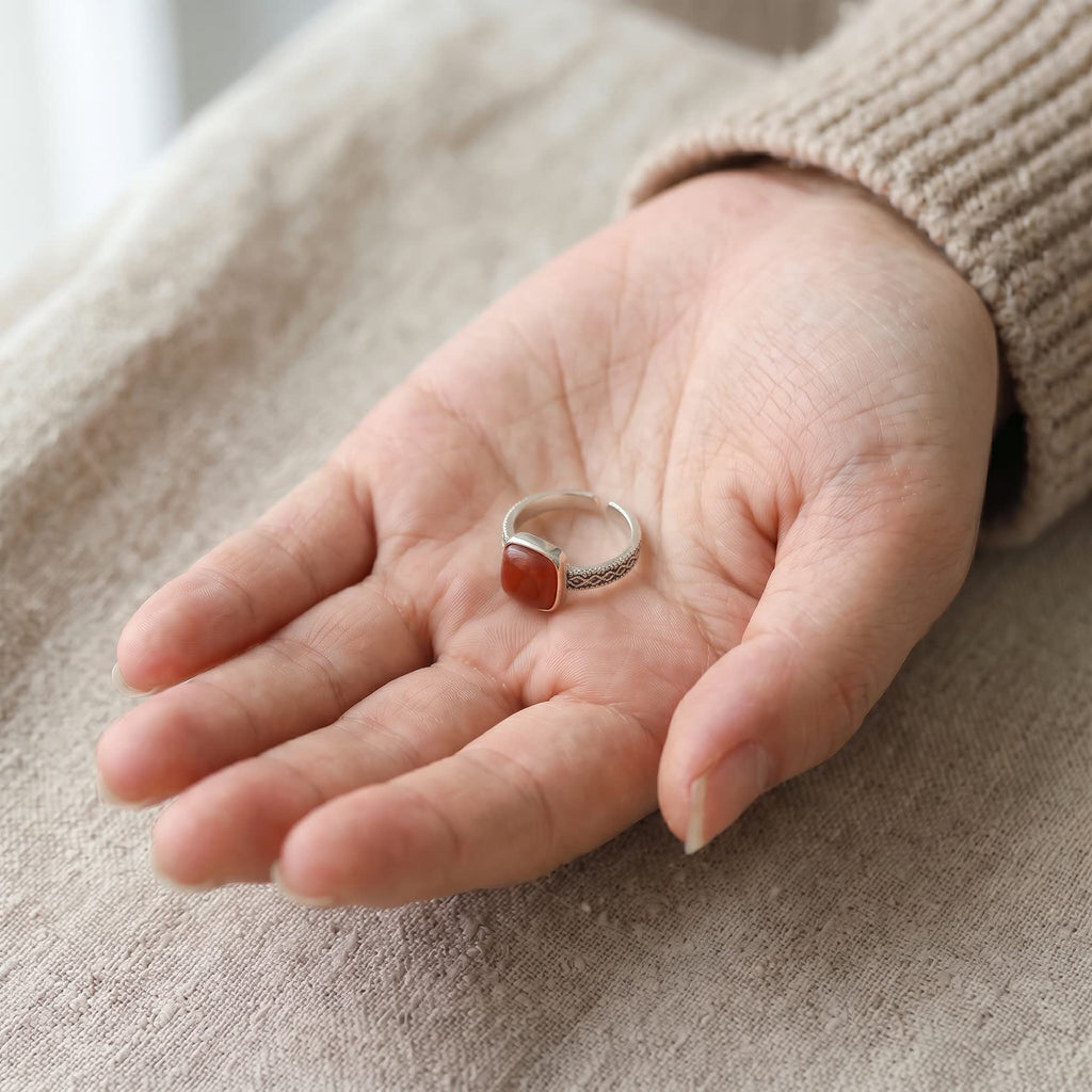 Openwork ring with a square red stone resting in an open palm to show its small size, adjustable open band visible