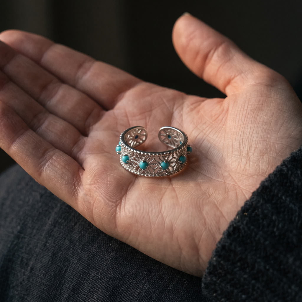 The openwork sterling silver ring standing in an open palm to show its size, a row of blue-green stones along the band