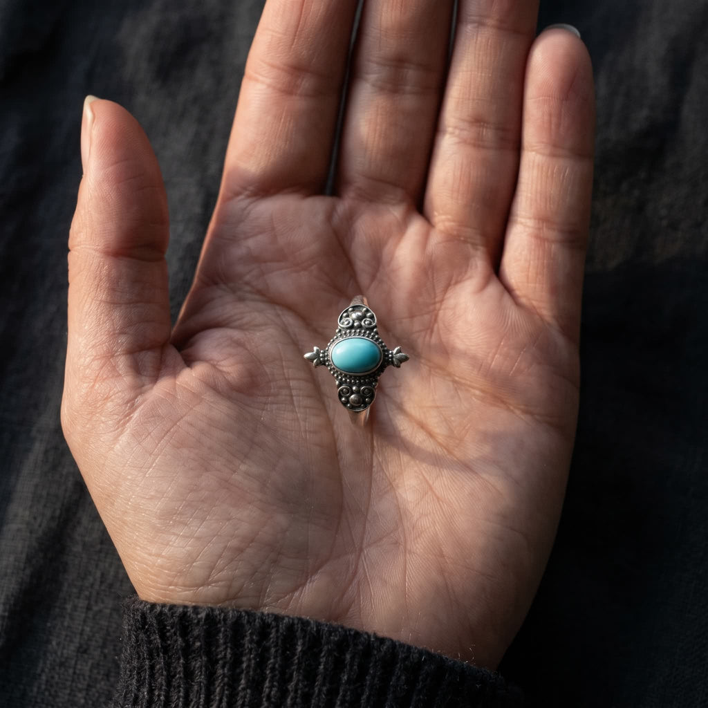 Small oval turquoise ring with granulated detailing standing in an open palm to show its size