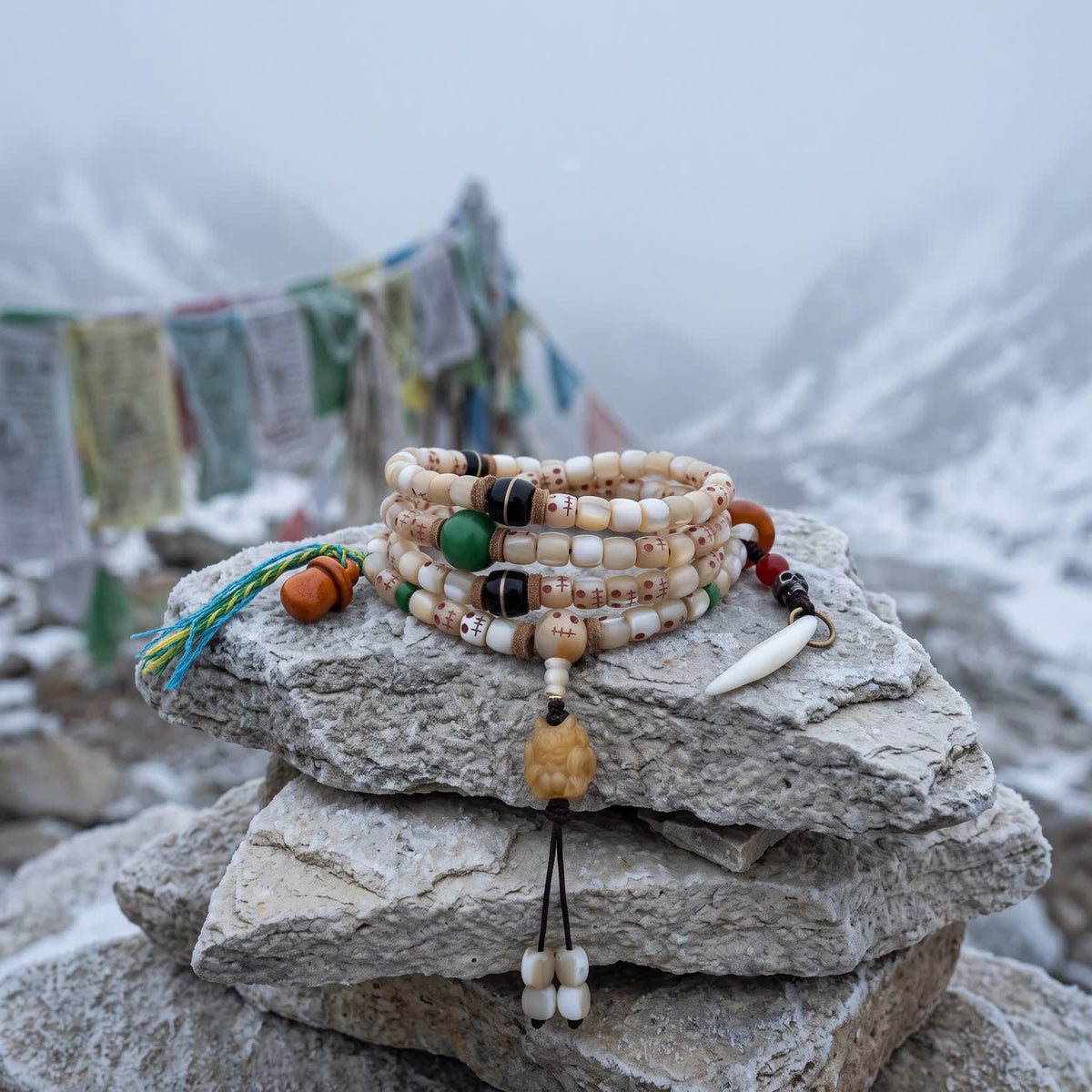 Fish bone mala on a frosted stone cairn in morning mist, faded prayer flags and snowy slopes blurred behind