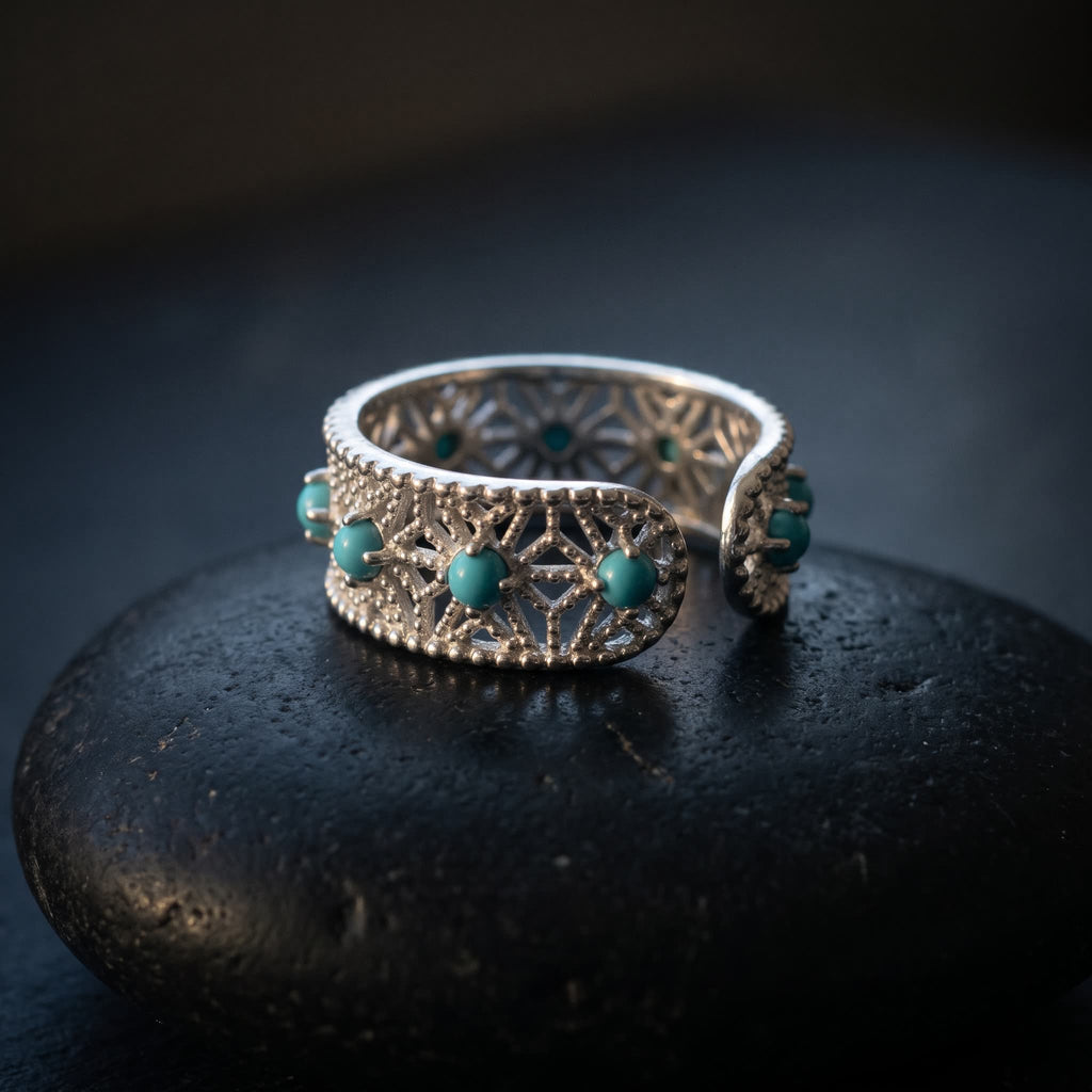 Openwork lace ring in 925 sterling silver with blue-green stones resting on a black river stone