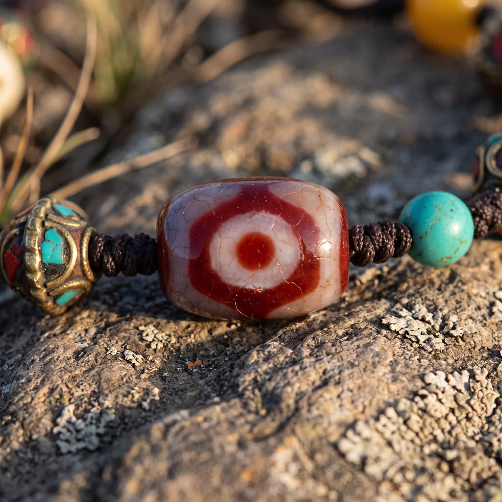 Close-up of the three-eyed red agate dzi bead with fine crackle lines, between a copper bead with red and blue-green inlay and a blue-green bead