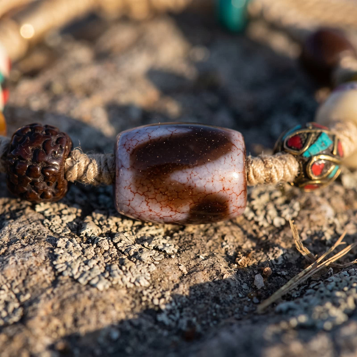 Close-up of the tiger-tooth pattern dzi bead with fine red-vein crackle, between a five-face rudraksha seed and a copper bead with red and blue-green inlay