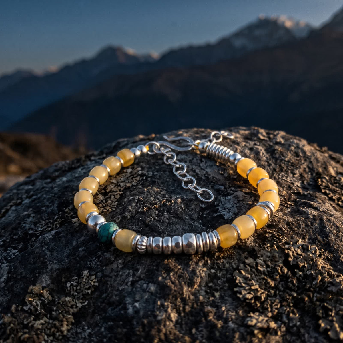 Honey-yellow bead and turquoise bracelet on a lichen-covered boulder at dusk with dark mountains behind