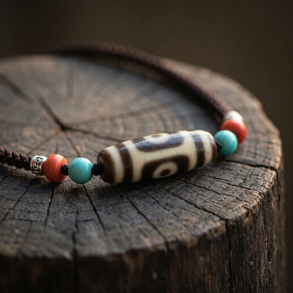 Agate dzi bead necklace with blue-green and red beads resting on the cracked top of a dark tree stump in low warm light
