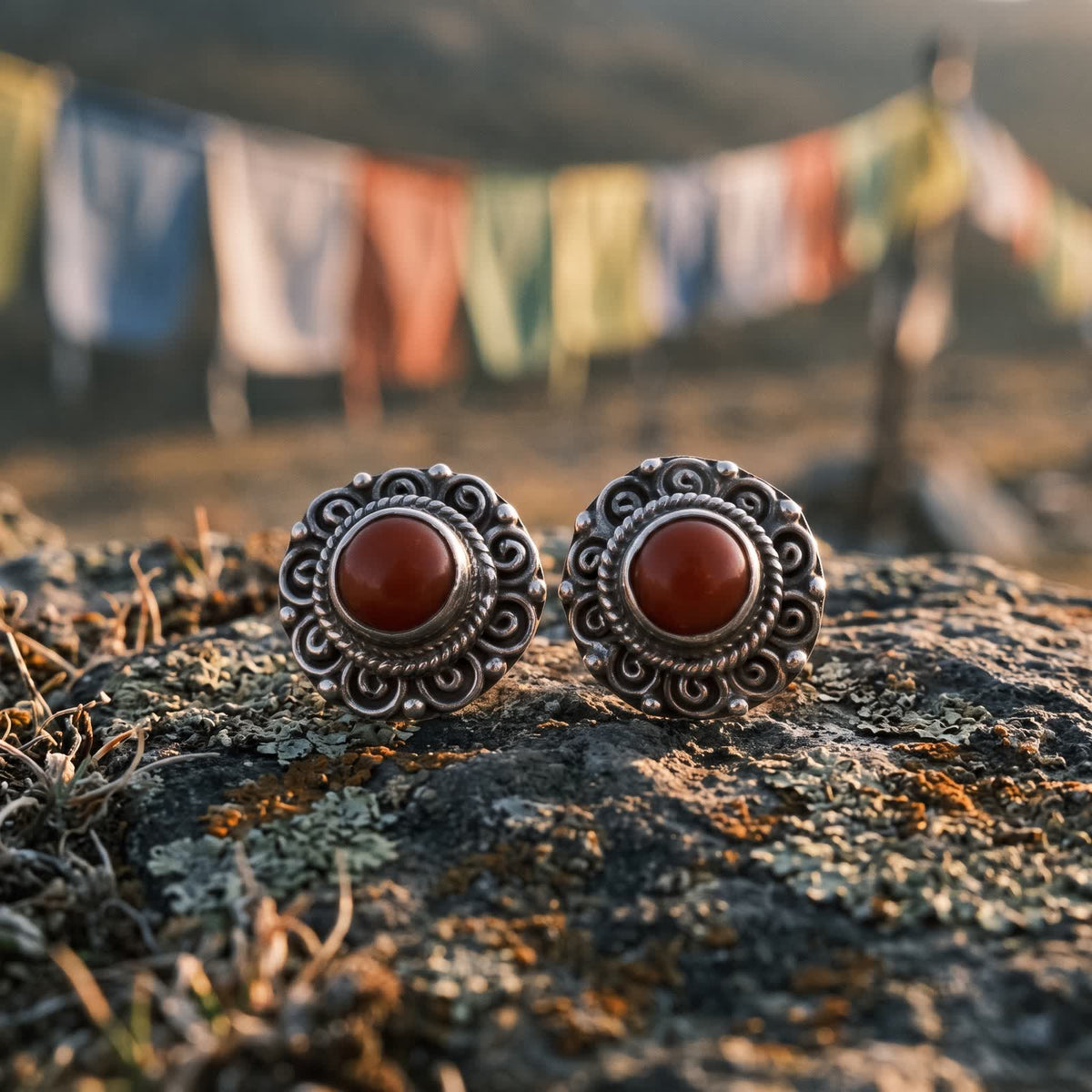 Red stone filigree stud earrings on a lichen-covered rock with prayer flags blurred behind