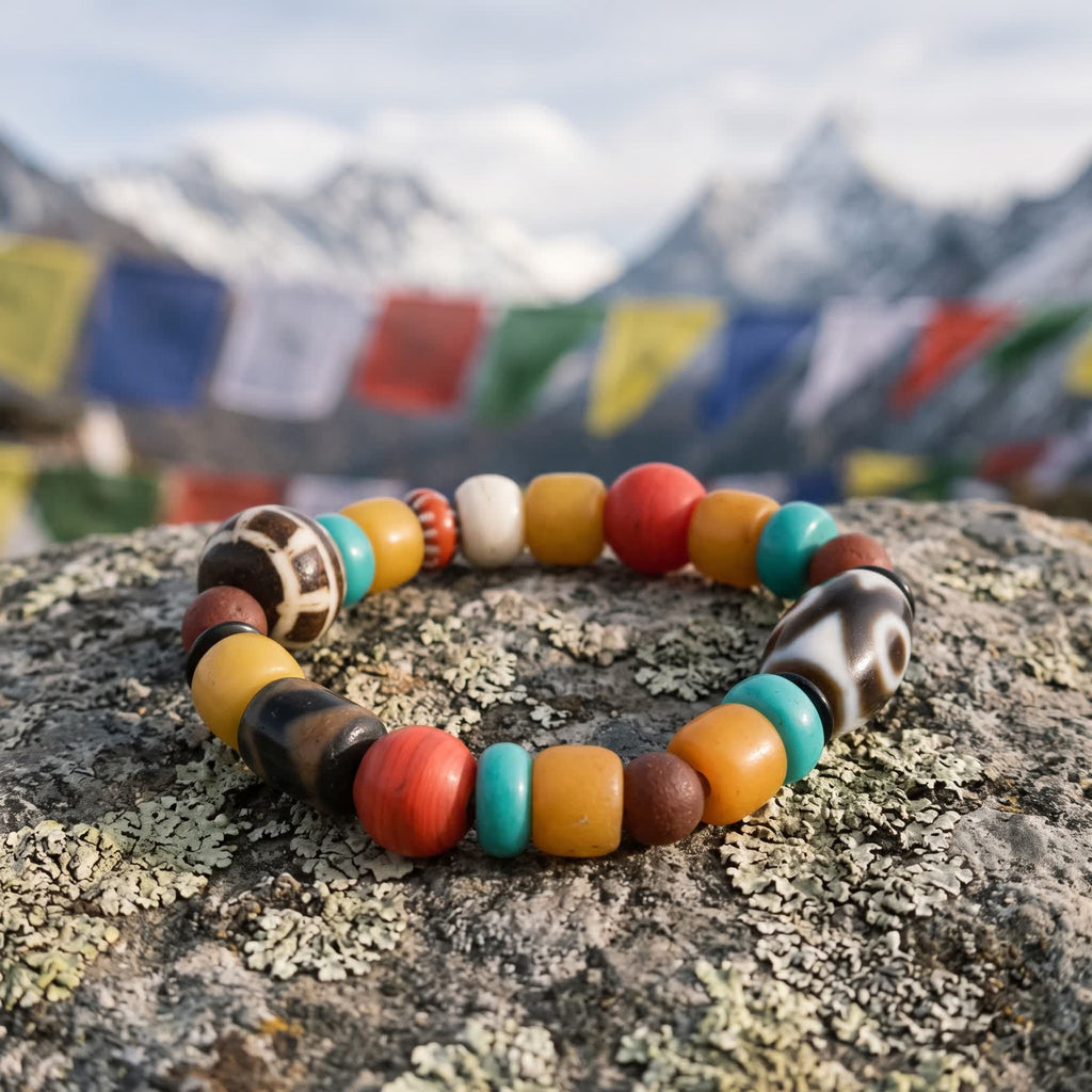 Multi-bead agate dzi bracelet on a lichen-covered stone with prayer flags and snow peaks blurred behind