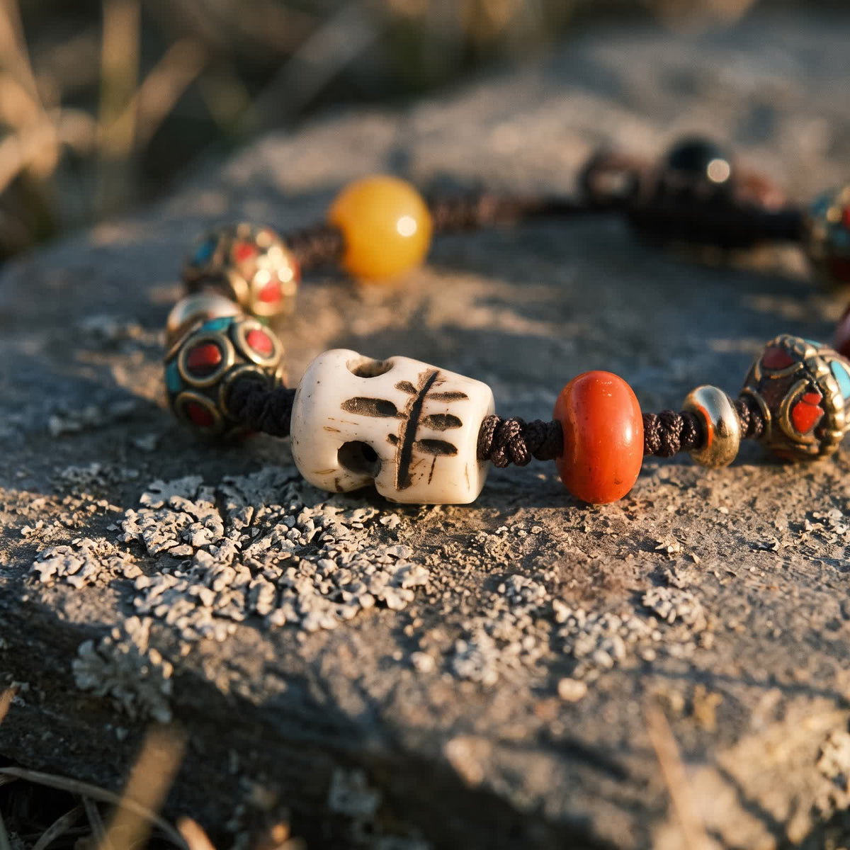 Close-up of the carved ox bone skull bead beside a red bead, a golden bead and copper beads with red and blue-green inlay