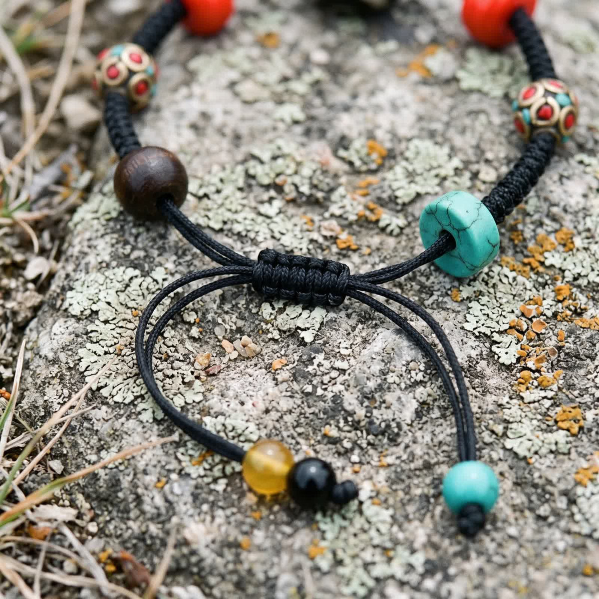 Close-up of the braided sliding knot where the cord tails meet, ending in yellow, black and blue-green beads, beside an agarwood bead and a blue-green disc