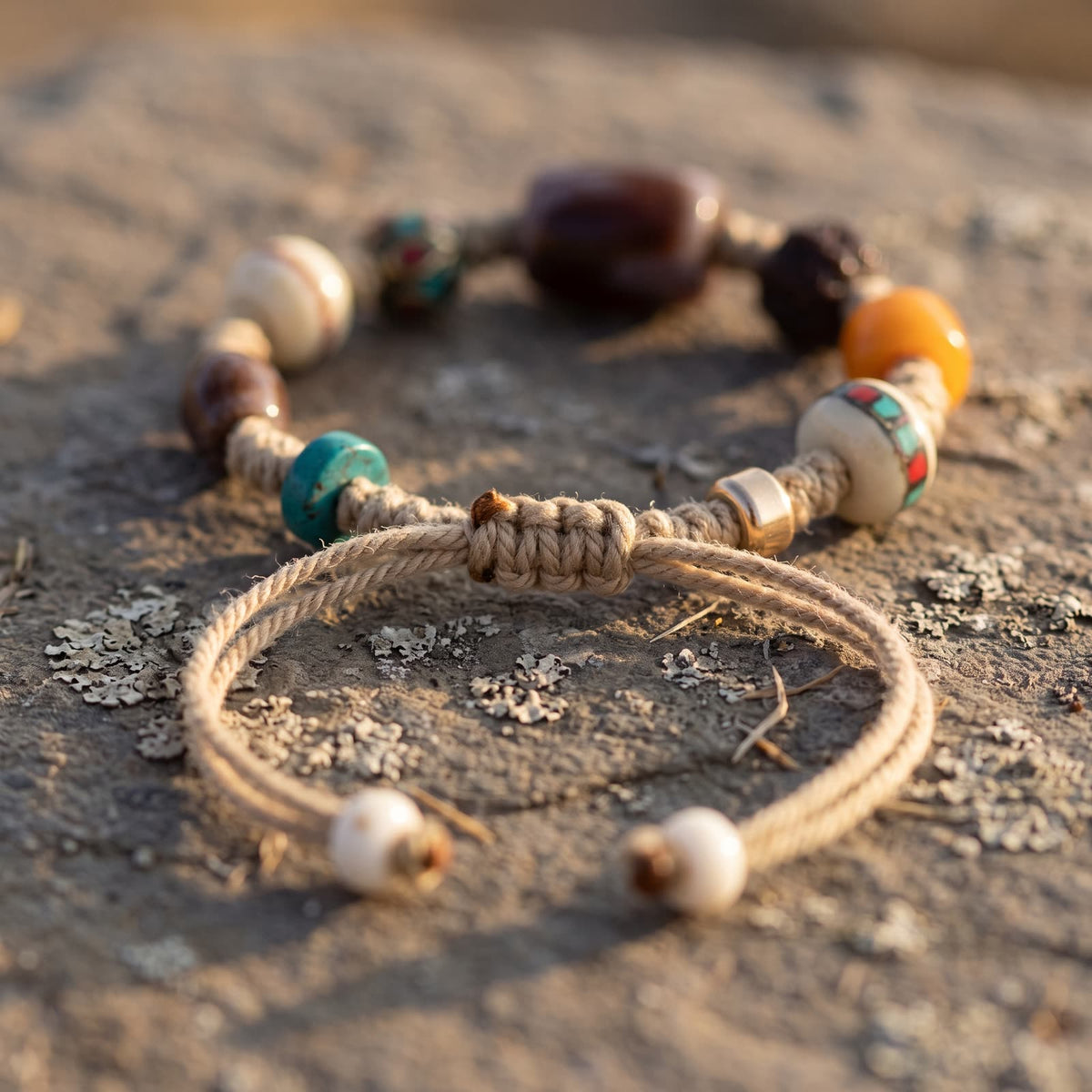 Close-up of the braided sliding knot and two cord tails ending in small white beads, beside a blue-green disc and a golden spacer