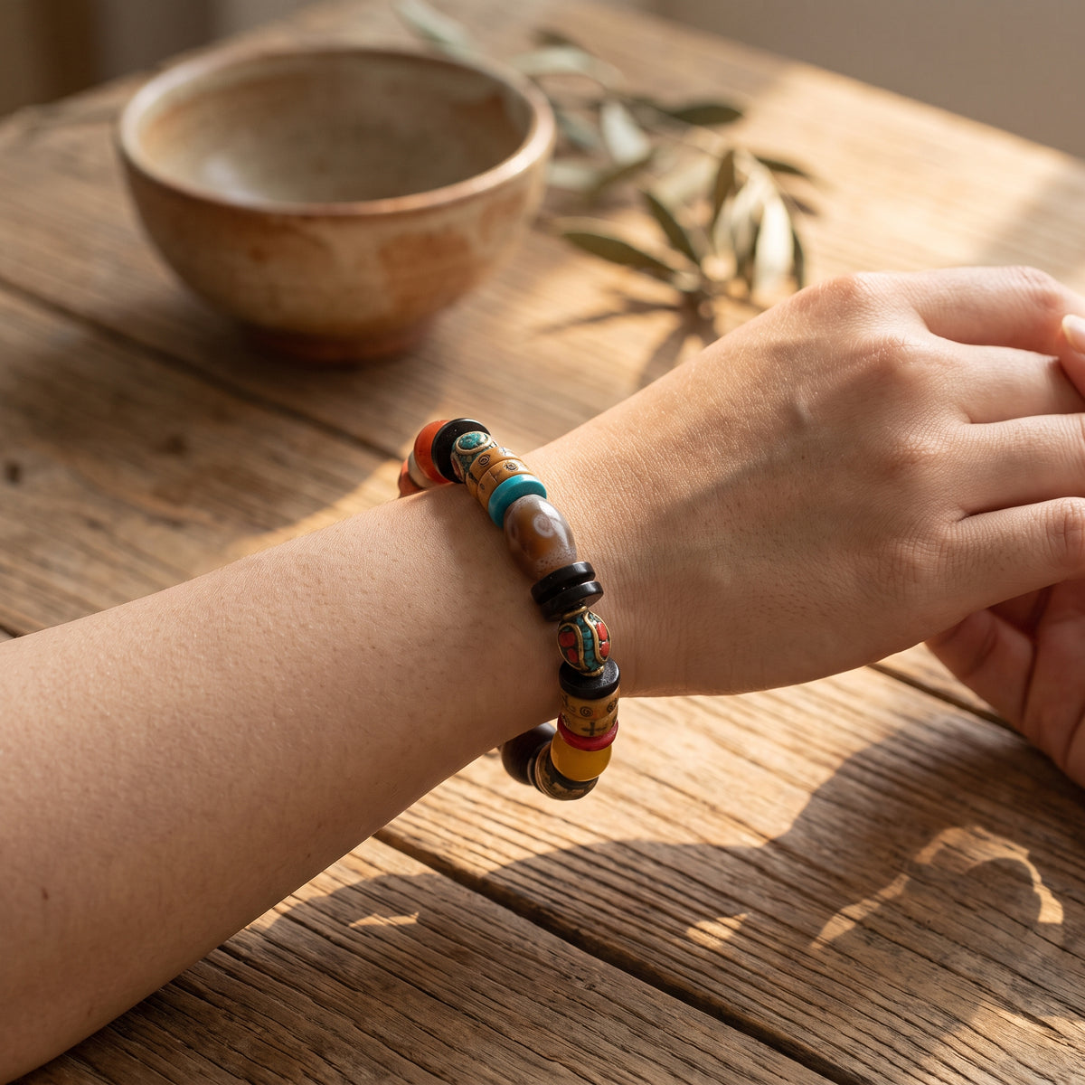 Wrist wearing a colorful mixed-bead bracelet, hands loosely clasped on a sunlit wooden table