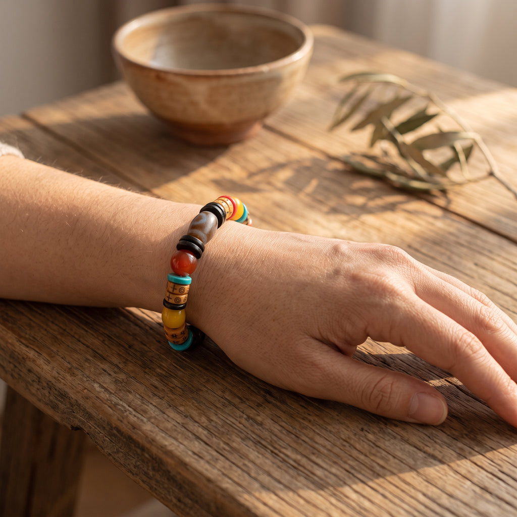 Mixed-bead bracelet on a wrist resting on a weathered wooden table, a small ceramic cup and olive sprig behind