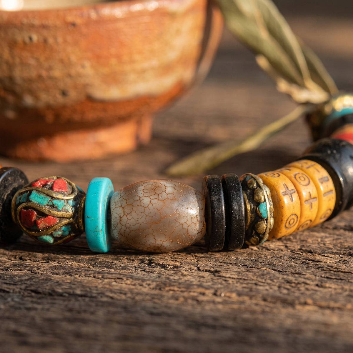 Detail of an inlaid turquoise-and-red metal bead, a turquoise disc and a crackled gray barrel bead between carved bone beads