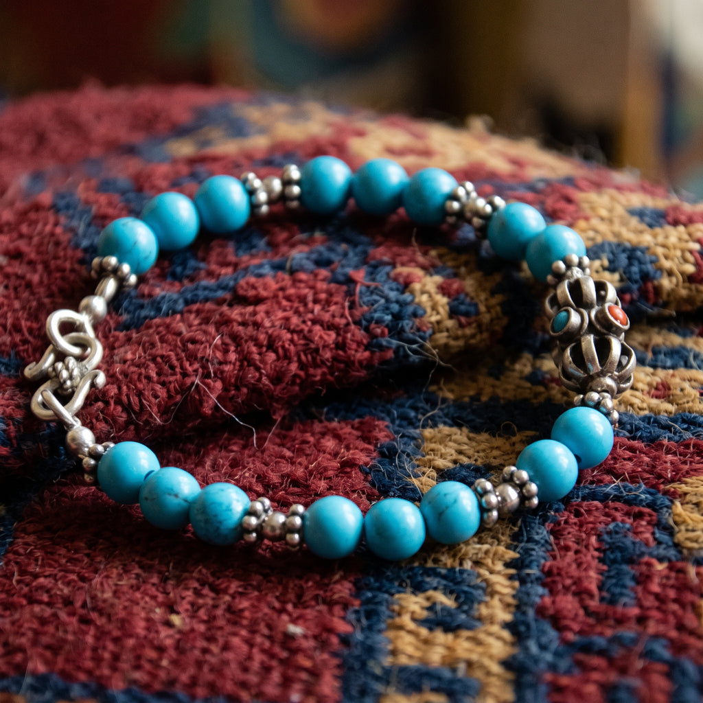Turquoise and silver vajra bracelet with a hook clasp, laid on a red and blue rug
