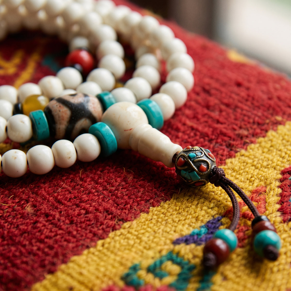 Close-up of a black and tan three-eyed dzi between turquoise discs, with the guru bead and tassel on a red rug