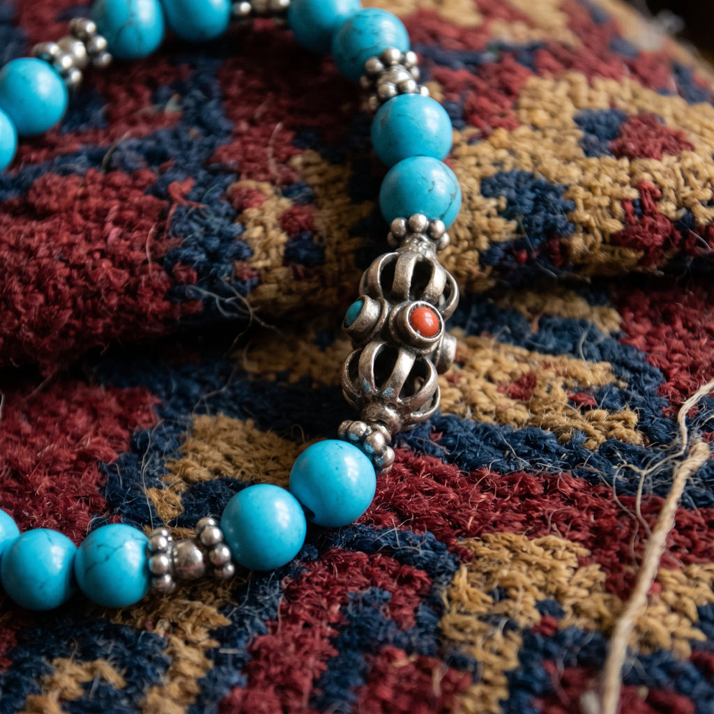 Close-up of the silver vajra and small beaded spacers between turquoise beads on a woven textile